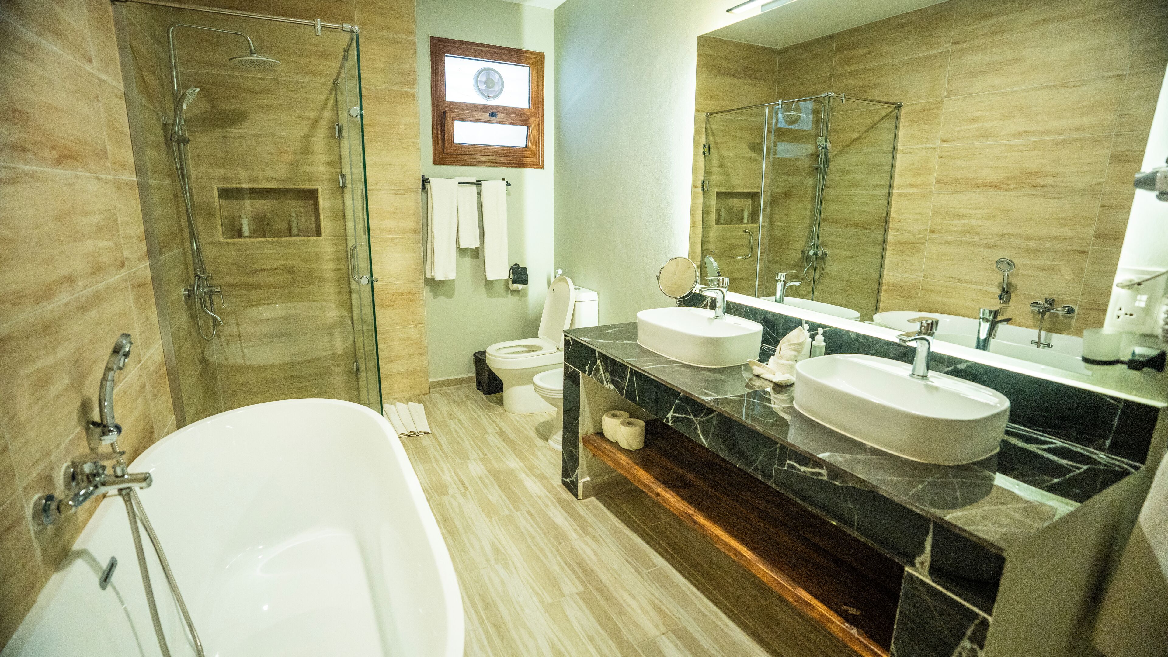 Un baño moderno con cabina de ducha de vidrio, dos lavamanos, un espejo grande y un inodoro.