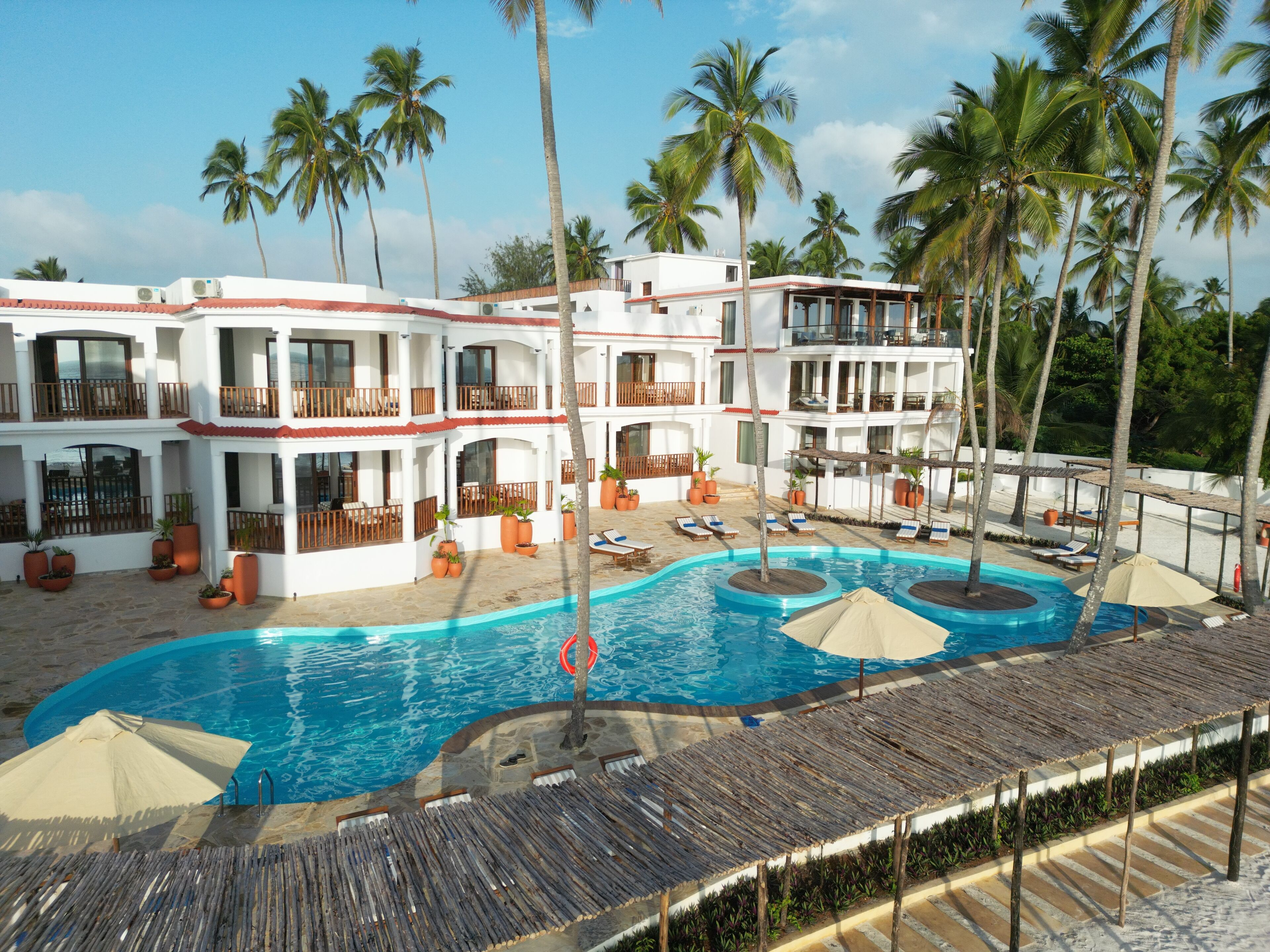 A resort with a large pool, multiple balconies, and palm trees.