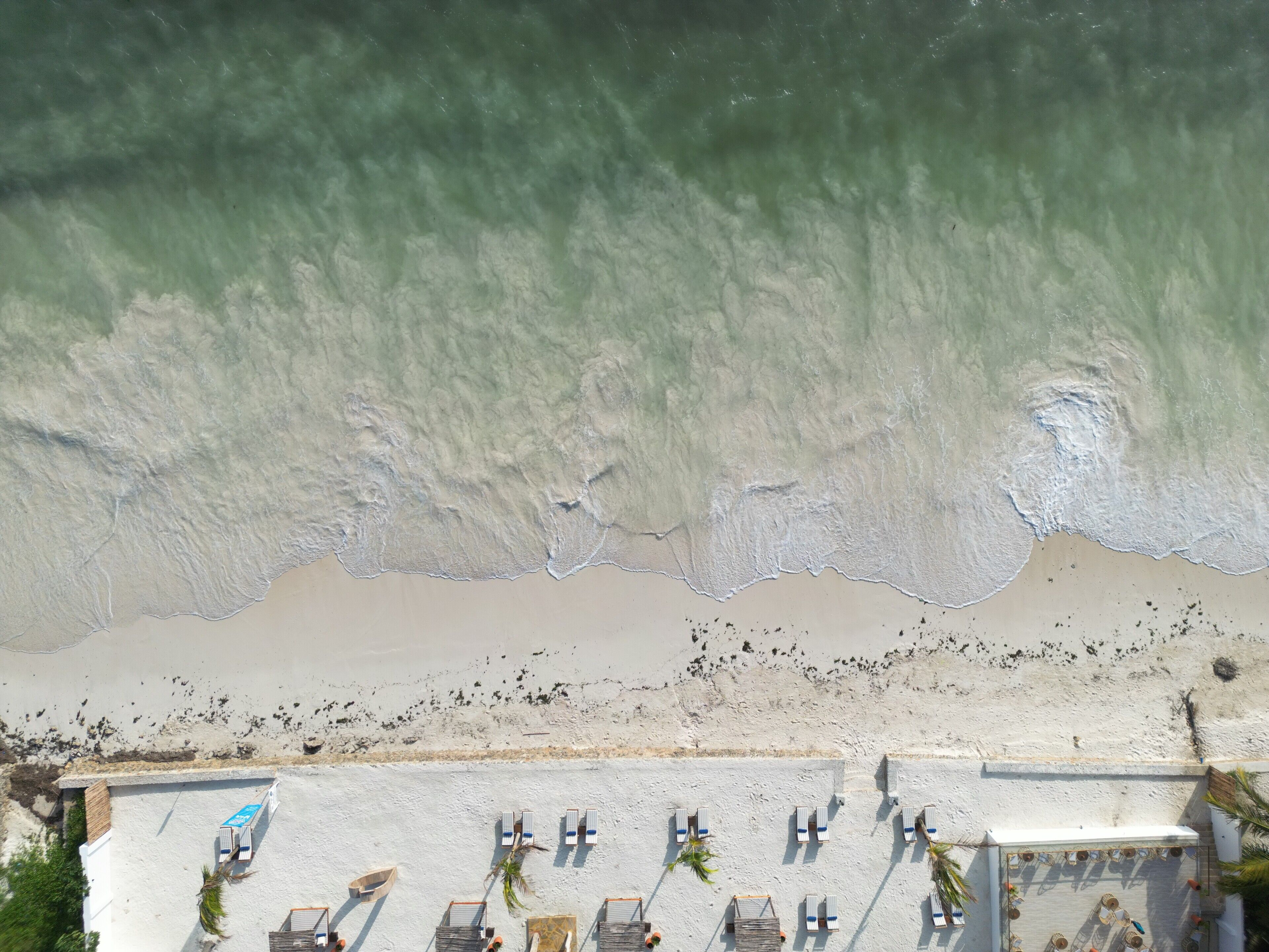 An aerial view of a beach with a row of sun loungers and a small boat.