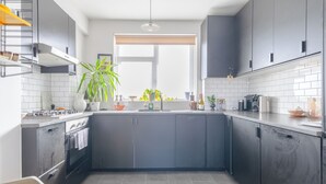 Une cuisine moderne avec des meubles de couleur sombre, une cuisinière à gaz, un évier et une fenêtre agrémentée de plantes.