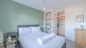 Un lit bien fait, avec du linge de lit blanc, une table de chevet avec des livres, une lampe et une étagère contenant divers objets.