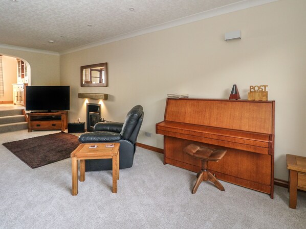 A living room with a television, a fireplace, a leather chair, a wooden coffee table, and a piano. - Dunira (Mallaig)