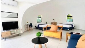A modern living room with a curved ceiling, a flat-screen TV, a sofa, a coffee table, and two beds with windows. - Almendra Beach Place (Los Cóbanos)