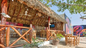 A rustic outdoor seating area with wooden furniture and thatched roofing. - Posada Las Coloradas (Rio Lagartos)