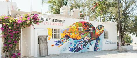 A building with a colorful mural of a sea turtle, a sign reading "HOTEL Y RESTAURANT LAS COLORADAS," and a white exterior.