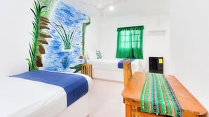 A room with two beds, a wooden table, a ceiling fan, a green curtain, and a wall mural. - Posada Las Coloradas (Rio Lagartos)