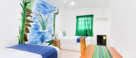 Una habitación con dos camas, una mesa de madera, un ventilador de techo, una cortina verde y un mural en la pared.