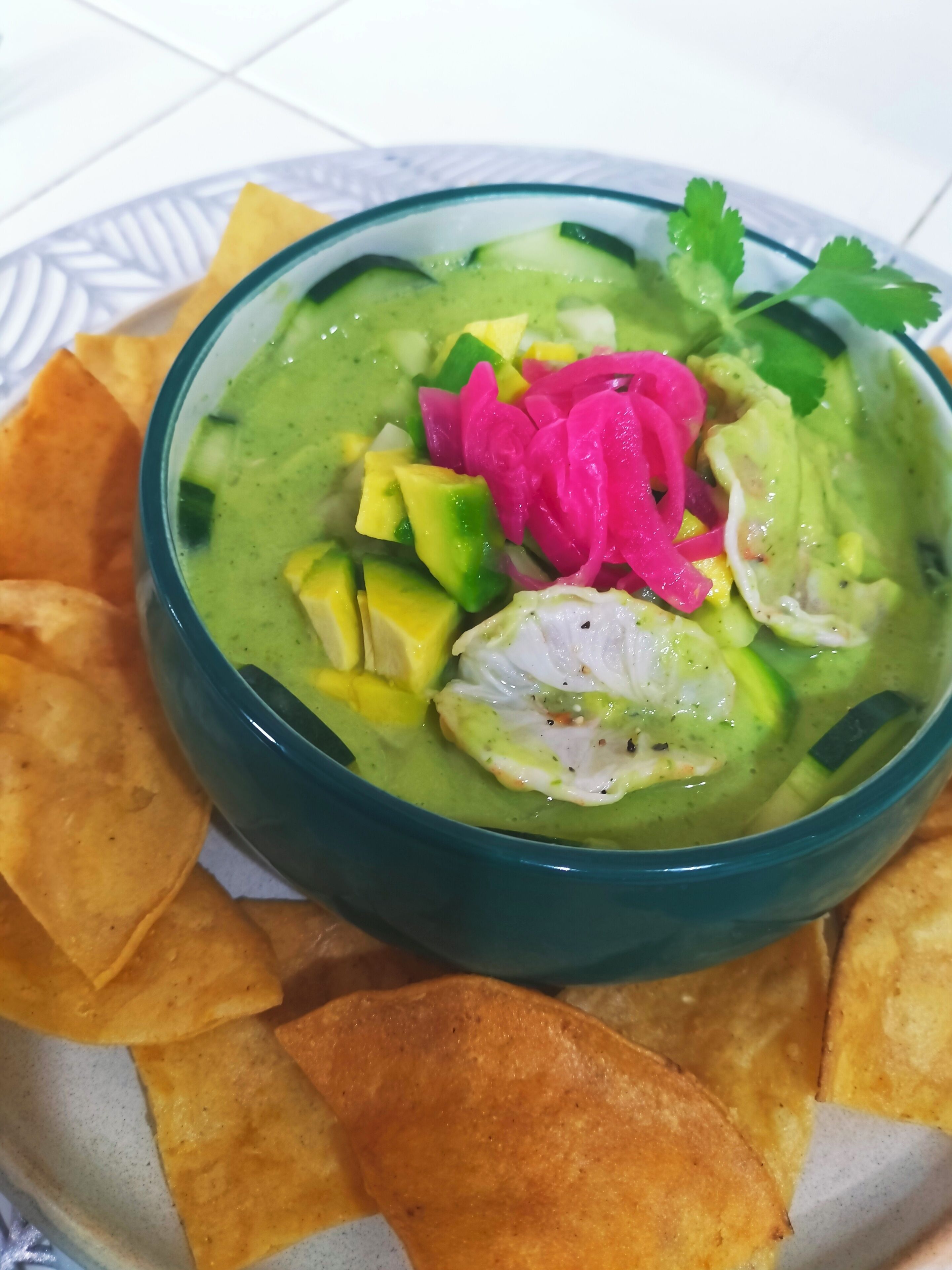 Un tazón de guacamole con trozos de aguacate, cebollas rojas encurtidas y un huevo escalfado, acompañado de totopos.