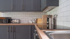 A modern kitchen with grey cabinets, a wooden countertop, a toaster, a kettle, and a knife block.