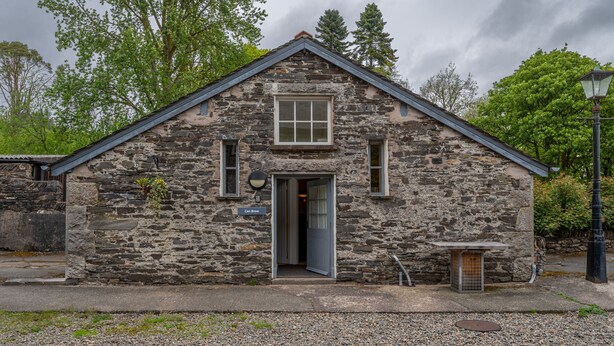 A stone building with a gabled roof, a door, and a small window.