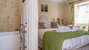 A bedroom with a bed, pillows, a green blanket, a white radiator, a picture on the wall, and a window with curtains.