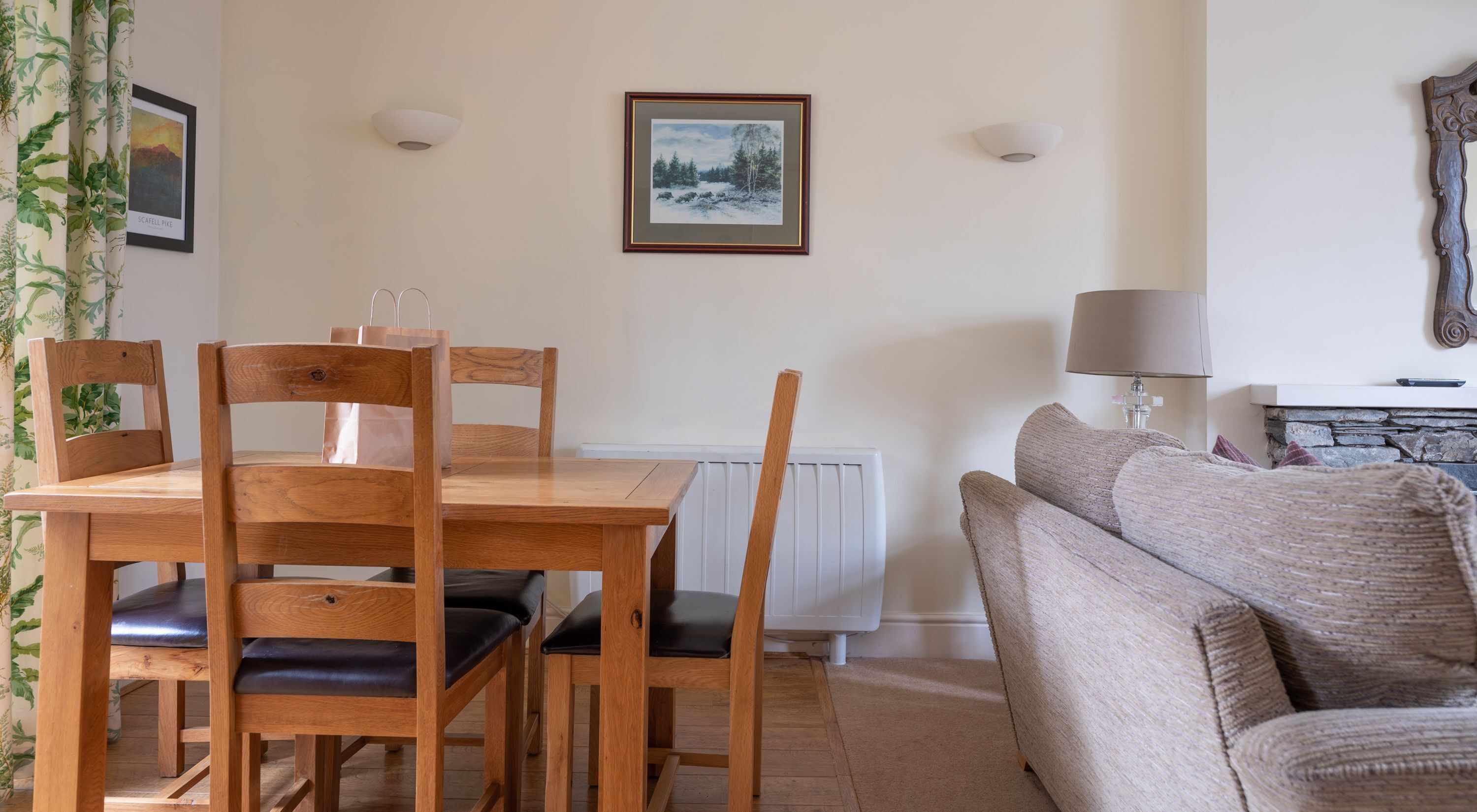 A dining area with a wooden table and chairs, a radiator, a framed picture on the wall, and a lamp.