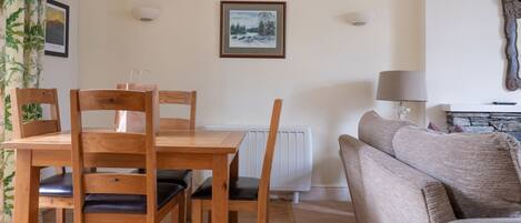 A dining area with a wooden table and chairs, a radiator, a framed picture on the wall, and a lamp.