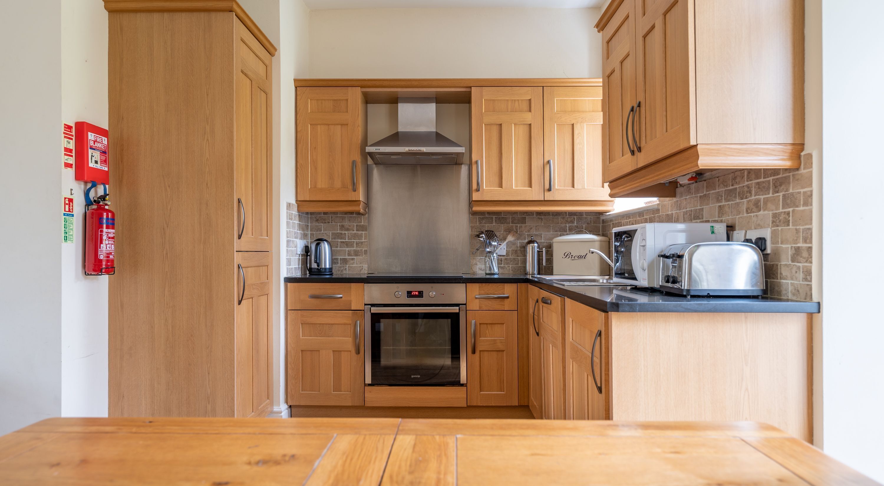 A kitchen with wooden cabinets, a stainless steel range hood, a built-in oven, and a toaster.