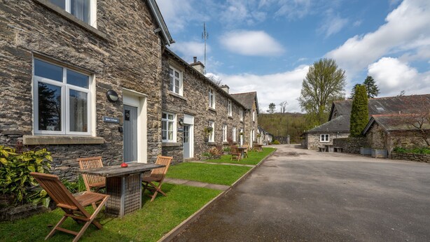 Une charmante maison en pierre avec une allée pavée, un espace extérieur aménagé pour s’asseoir et un ciel dégagé.