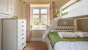 Une chambre avec un lit superposé, une commode, une fenêtre avec des rideaux et une vue sur l’extérieur.