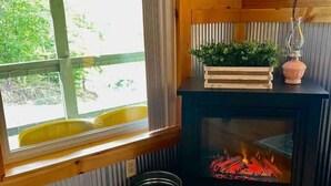 A cozy room with a fireplace, a window with a view, and a small wooden table. - Secluded 12-Acre Retreat w/ Hot Tub, Mountain Views, Arcade - Red River Gorge (Campton)