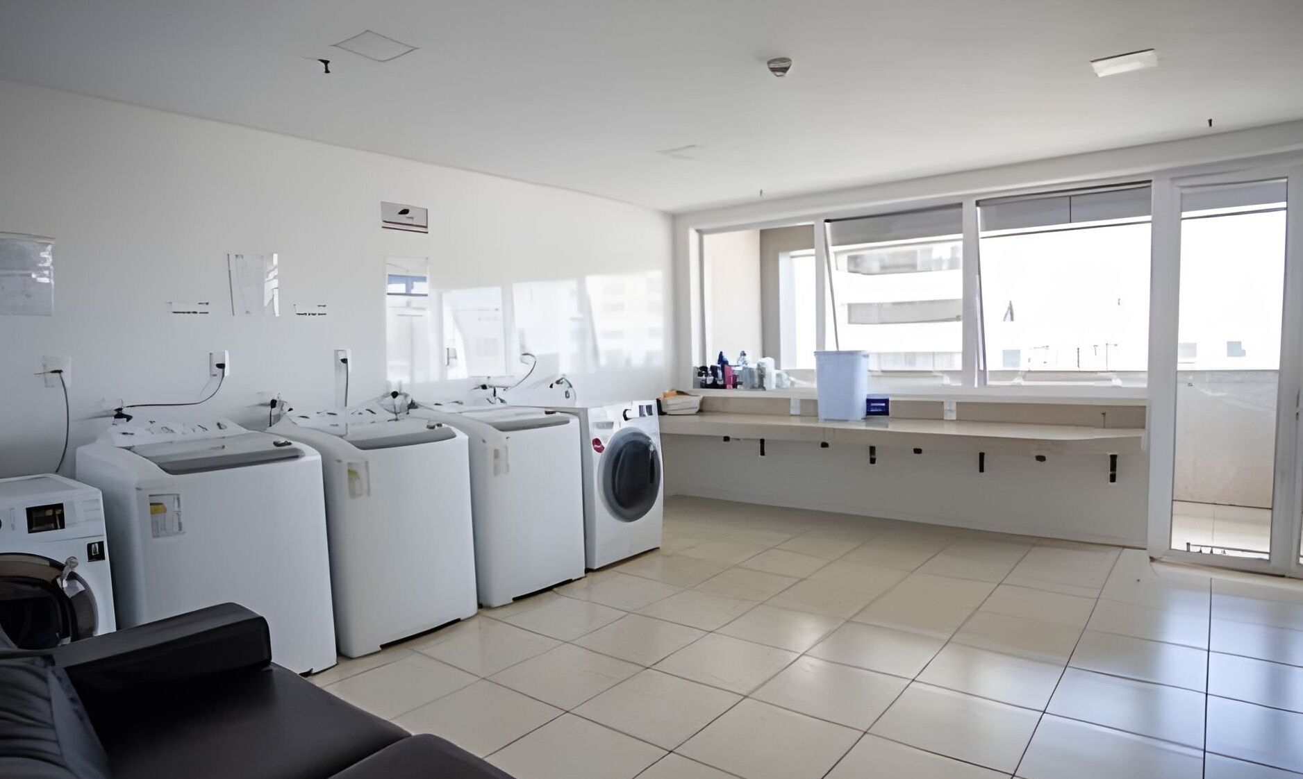 A laundry room with multiple washing machines, a bench, and a window with a view of the outside.