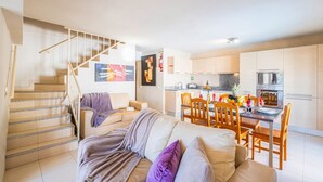Un apartamento moderno con una escalera que conduce a un dormitorio tipo loft, un comedor con sillas de madera y una cocina equipada con electrodomésticos de acero inoxidable.