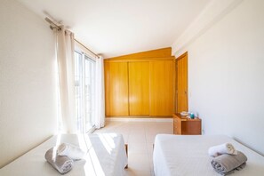 A hotel room with a bed, a wooden wardrobe, a small table with toiletries, and a window with curtains.