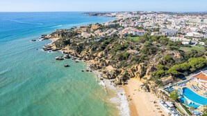 Vista aérea de un pueblo costero con playa, acantilados rocosos y un complejo de piscinas.