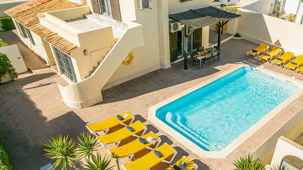Una piscina en la azotea con sillones de descanso amarillos, una zona de comedor y una escalera que sube a un nivel superior.