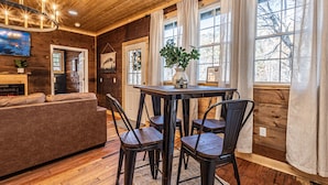 A cozy wooden interior with a sofa, dining table, chairs, and a fireplace. - Little Blue, cozy cabin with hot tub, fire pit, and cornhole near Polar Express (Bryson City)