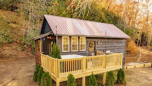 A rustic cabin with a wooden deck, a porch, and a metal roof. - Little Blue, cozy cabin with hot tub, fire pit, and cornhole near Polar Express (Bryson City)