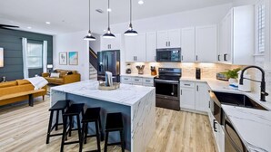 Une cuisine moderne avec des meubles blancs, un îlot en marbre, des tabourets de bar noirs et un four encastré.