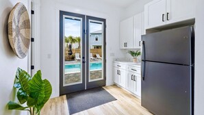 Une cuisine moderne avec des meubles blancs, un réfrigérateur noir et une vue sur une piscine, visible à travers des portes vitrées.