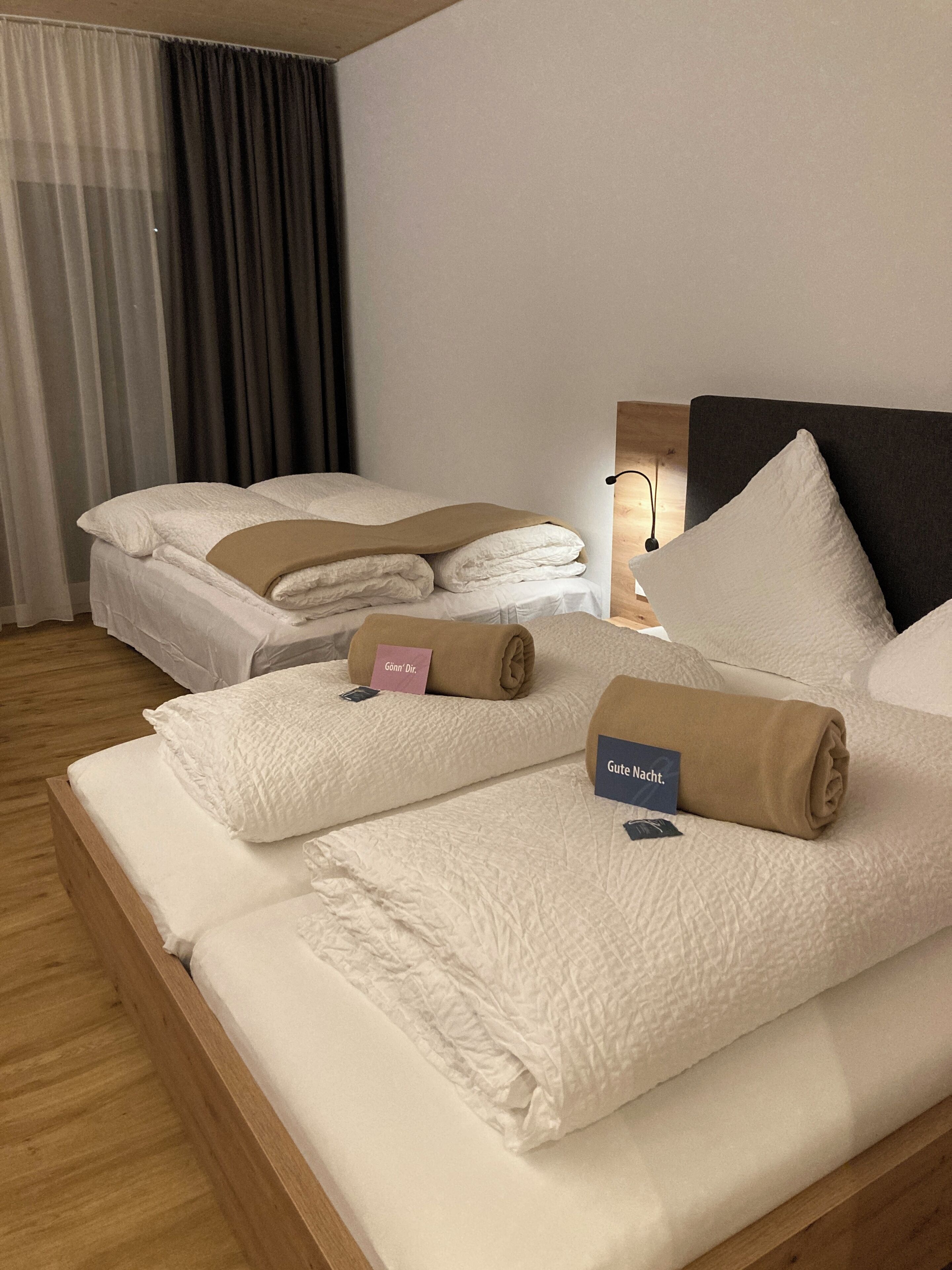 A hotel room with a large bed, a bedside table with a lamp, and a window with curtains.