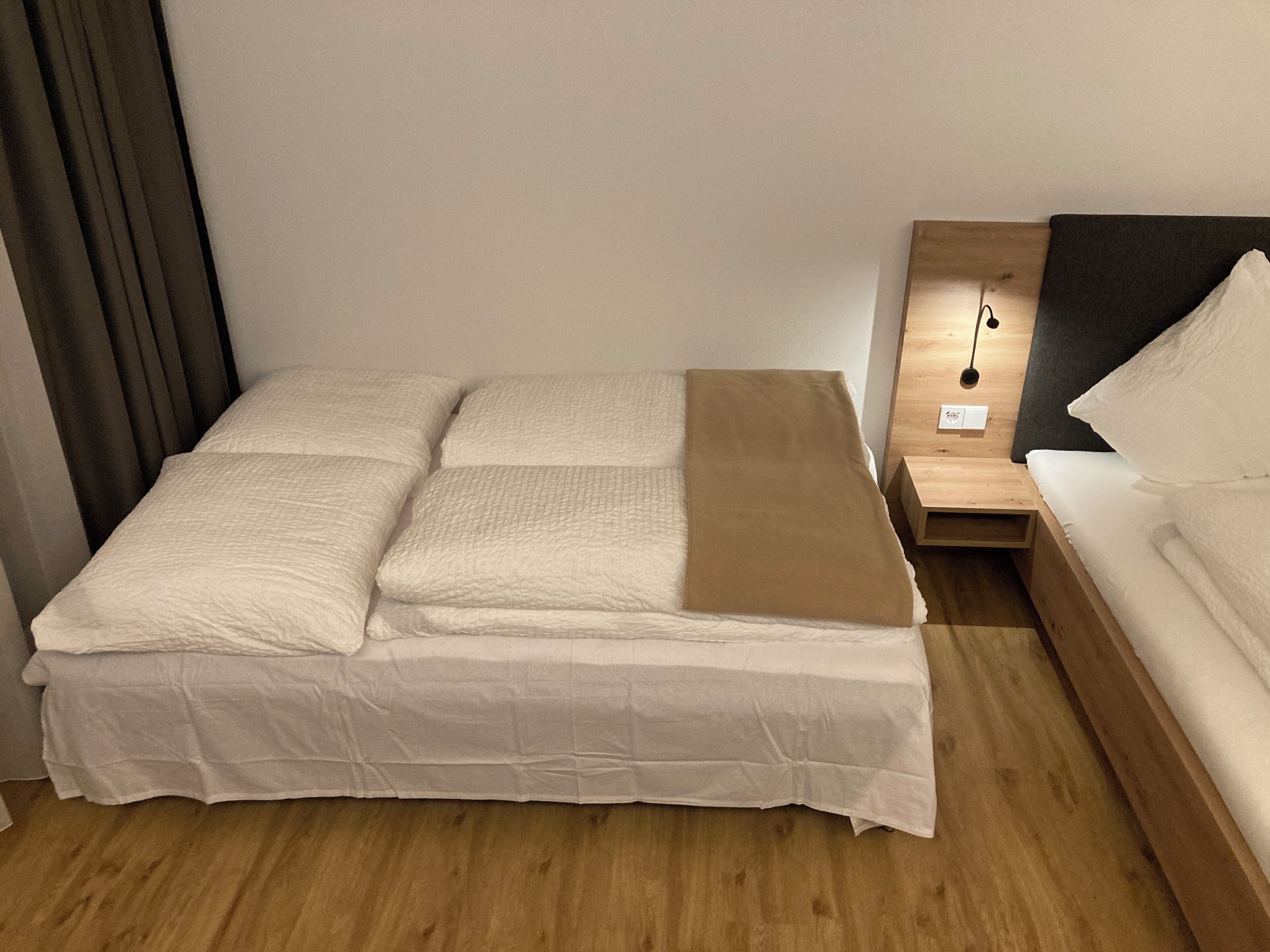 A neatly made bed with a white mattress and pillows, a brown blanket, and a wooden nightstand with a lamp.
