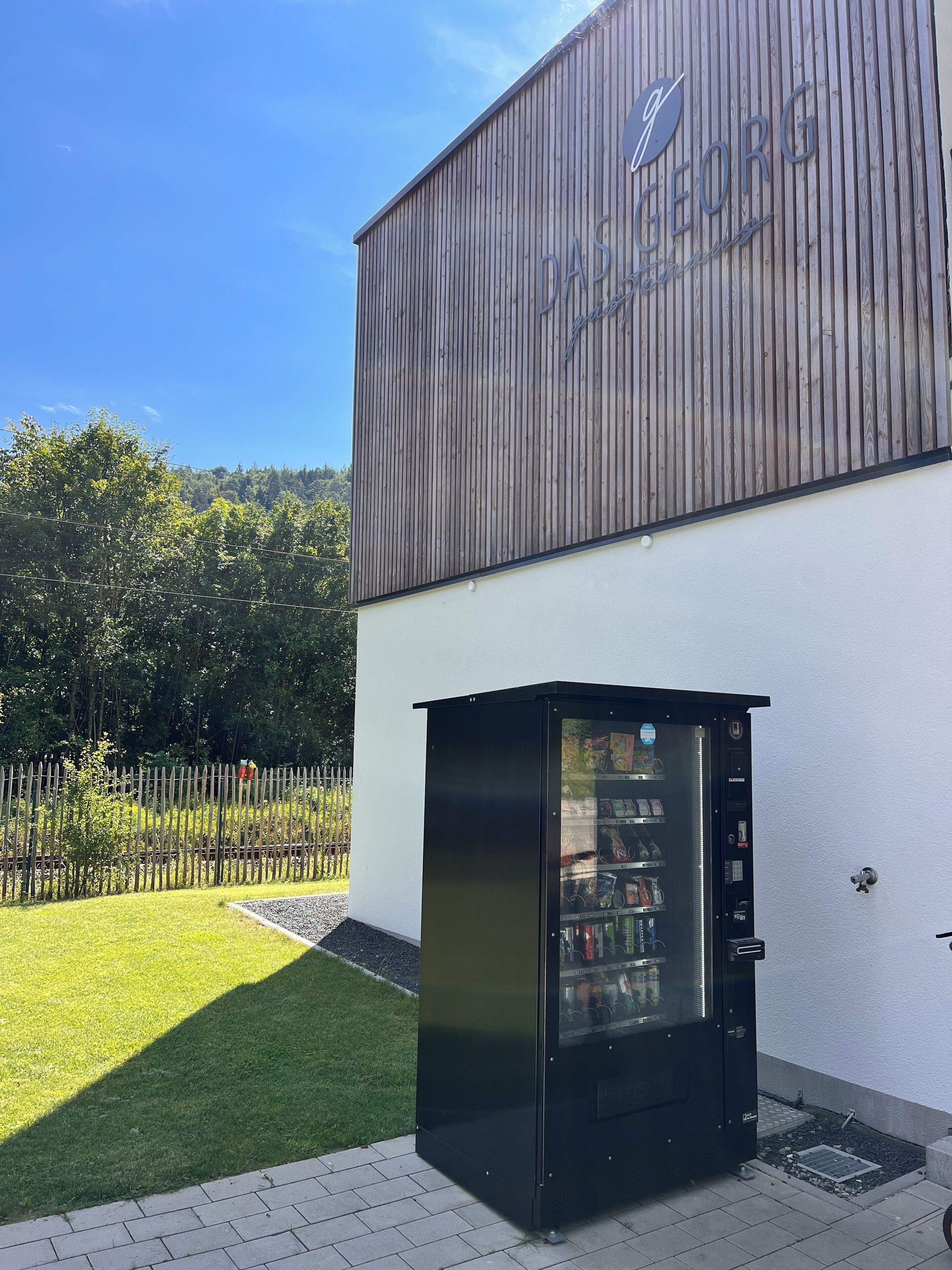 A vending machine outside a building with a wooden facade and a sign that reads "DAS GEORG".