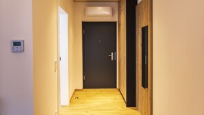 Un pasillo estrecho con suelo de madera, una puerta al final y un equipo de aire acondicionado en la pared.