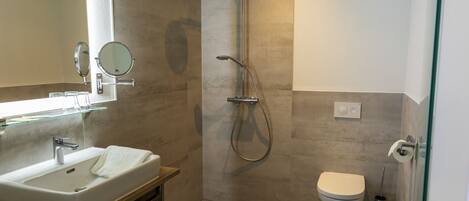 Een moderne badkamer met een groot wastafel, spiegel, douche en toilet.