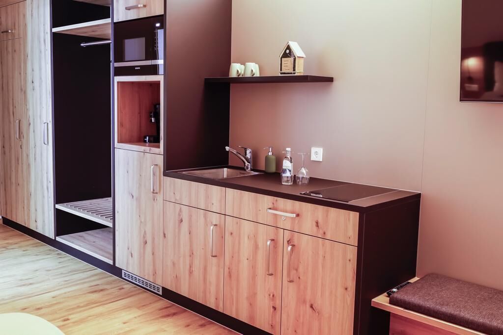 Una cocina moderna con armarios de madera, microondas integrado y una encimera con lavabo y artículos de aseo.