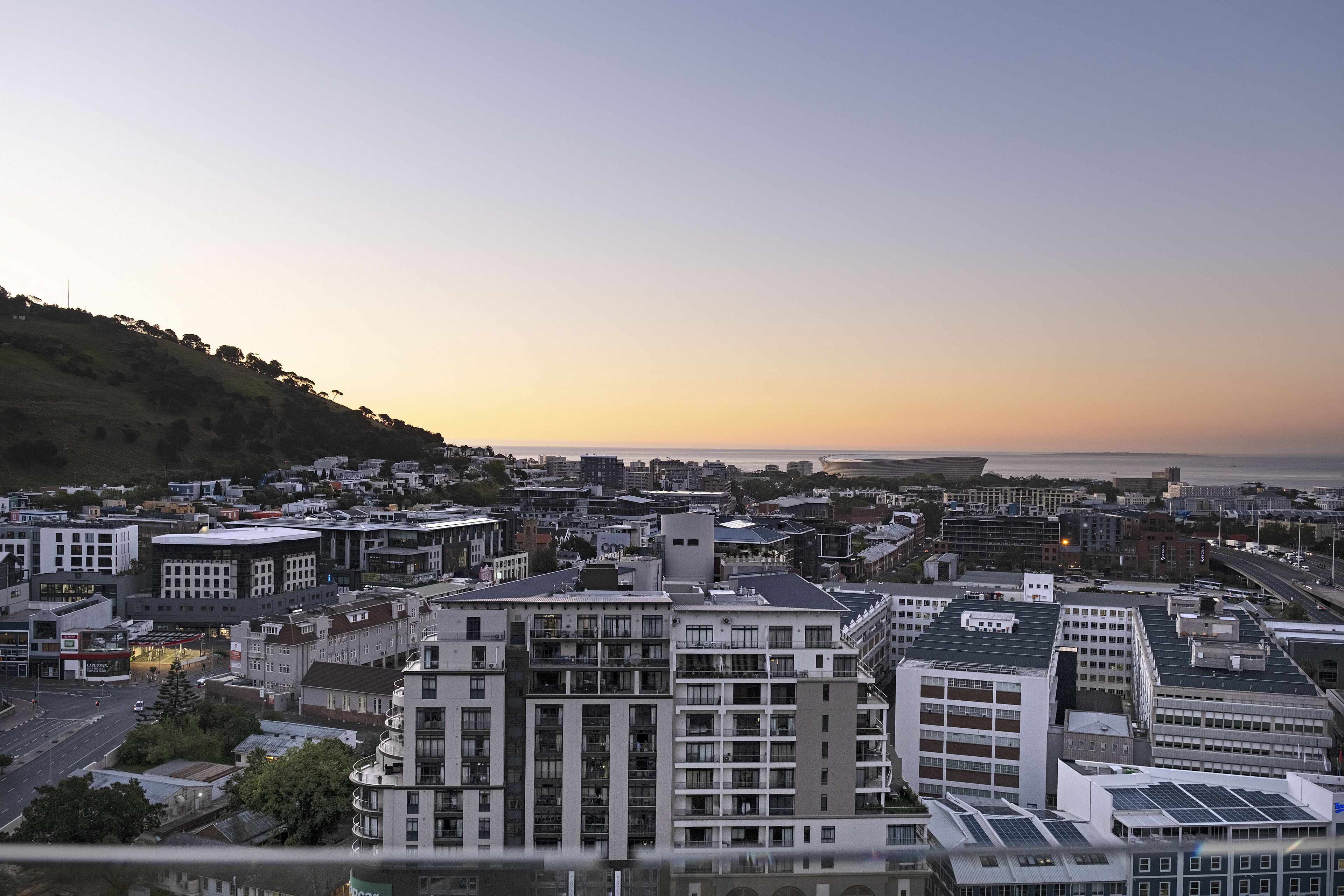 A cityscape with modern buildings, a waterfront, and a hilly backdrop.