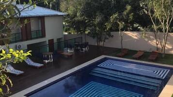 A swimming pool with geometric tile patterns, surrounded by a grassy area and a building with a sloped roof.