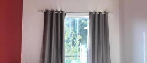 Un dormitorio con cama, ventana con cortinas, techo de madera y una lámpara colgante.