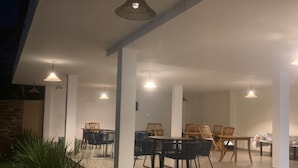 An outdoor patio area with tables and chairs, surrounded by white pillars and hanging lights. - Foca Guest House (Búzios)