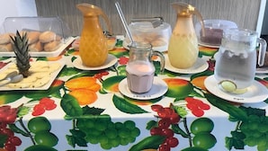 A breakfast buffet with various food items and beverages on a table with a fruit pattern. - Foca Guest House (Búzios)