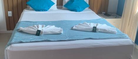 A hotel room with a large bed, two blue pillows, a blue blanket, and neatly folded towels.