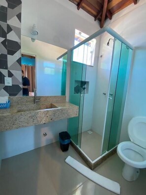 Un baño moderno con ducha envuelta en vidrio, encimera de granito y retrete blanco.