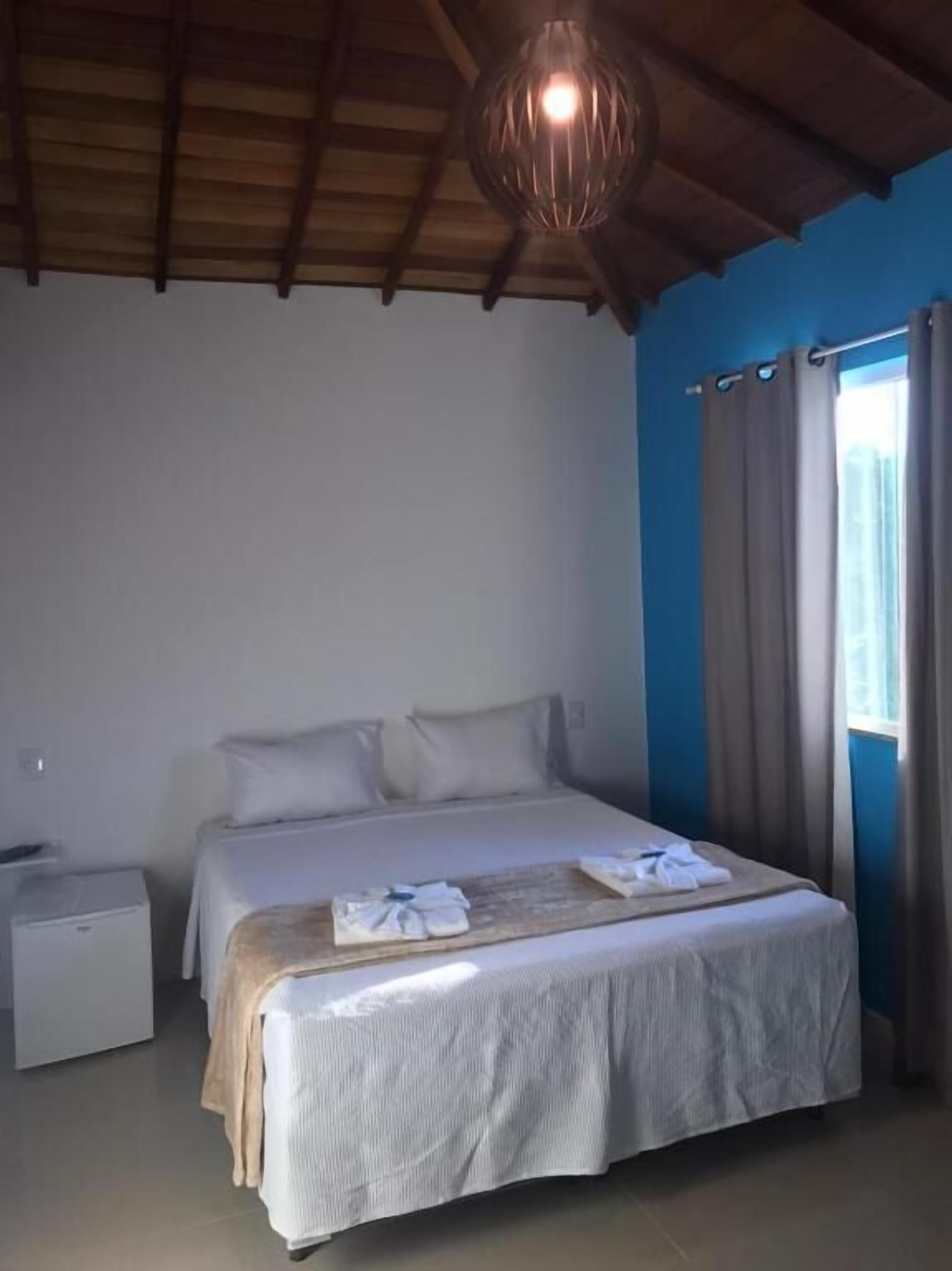 Un dormitorio con una cama grande, una mesita de noche, una lámpara en el techo y una ventana con cortinas.