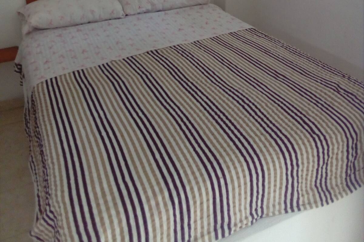 Un dormitorio con cabecera de madera, colcha a rayas y ventana con cortinas.
