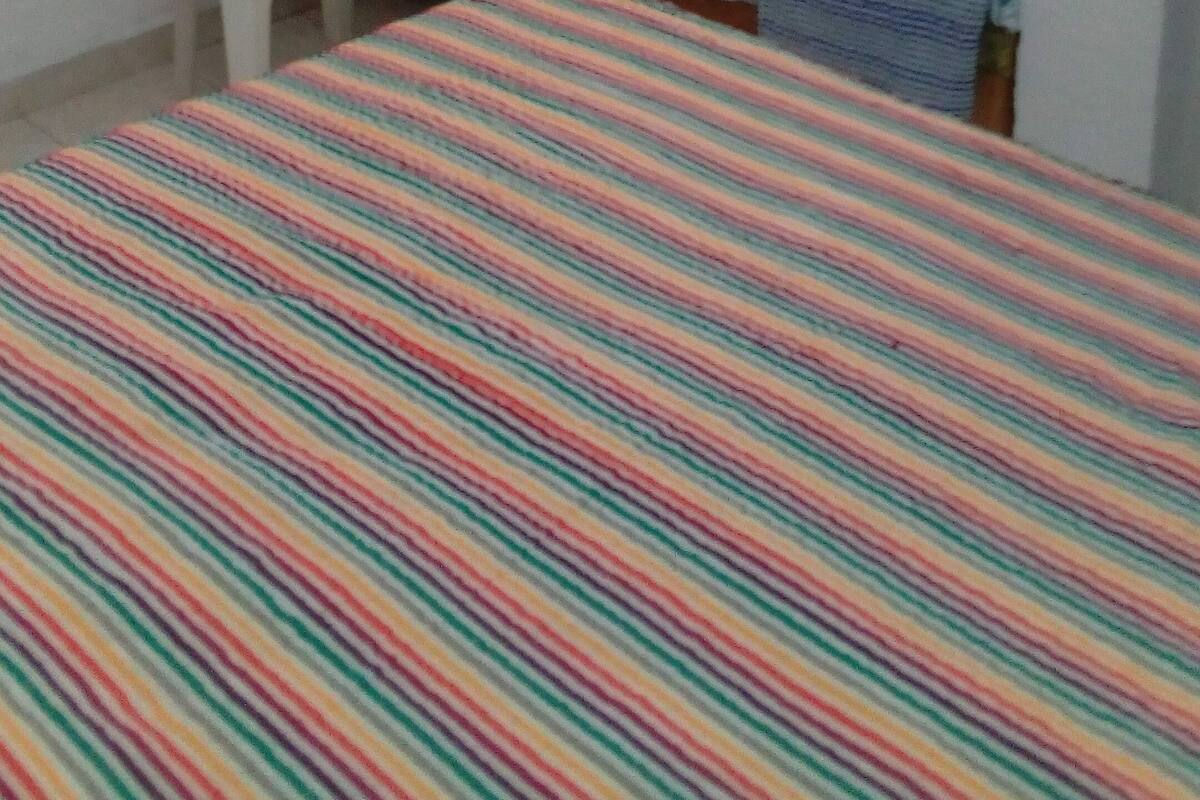 Una habitación pequeña y escasamente amoblada, con una cama, una silla y un televisor fijado a la pared.