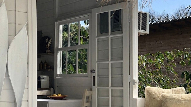 A cozy, white-walled room with a dining area, a wicker chair, and a bench with cushions. - Chalé Super Charmoso - CasaIvan (Florianópolis)