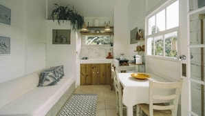 A cozy kitchen with white walls, wooden cabinets, and a dining area with a white table and chairs. - Chalé Super Charmoso - CasaIvan (Florianópolis)