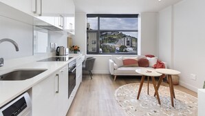 A modern kitchen with a large window, a dining area with a round table, and a sofa with cushions. - The Tokyo 701 (Cape Town)