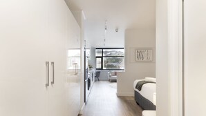 A modern, well-lit hallway leading to a bedroom with a large window, a washing machine, and a dining area. - The Tokyo 701 (Cape Town)